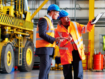 Two men in suits on a job-site wearing safety hats and orange construction vests